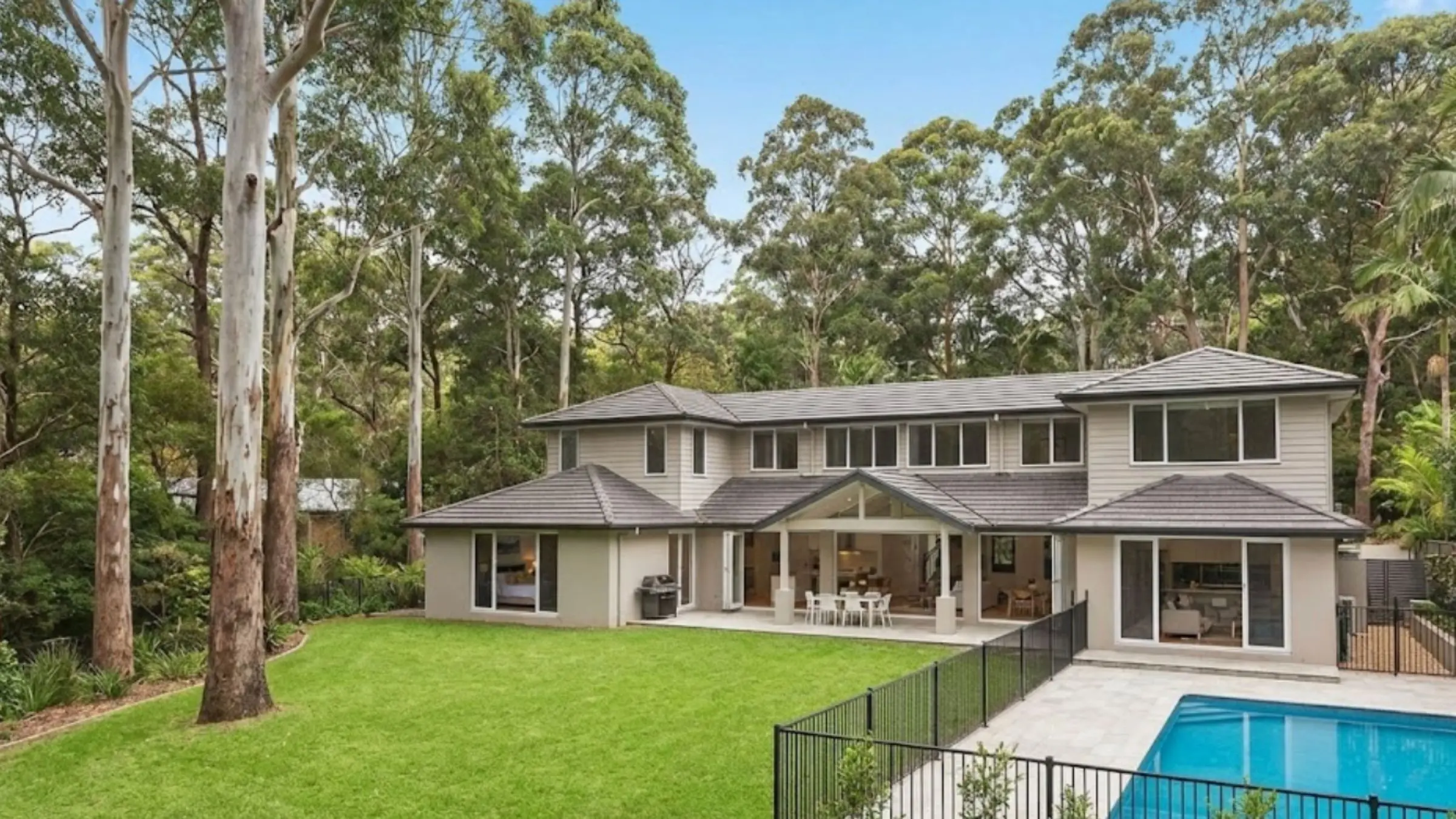 A spacious modern family home in Turramurra featuring a large backyard with a pool, set against a backdrop of tall gum trees and natural bushland