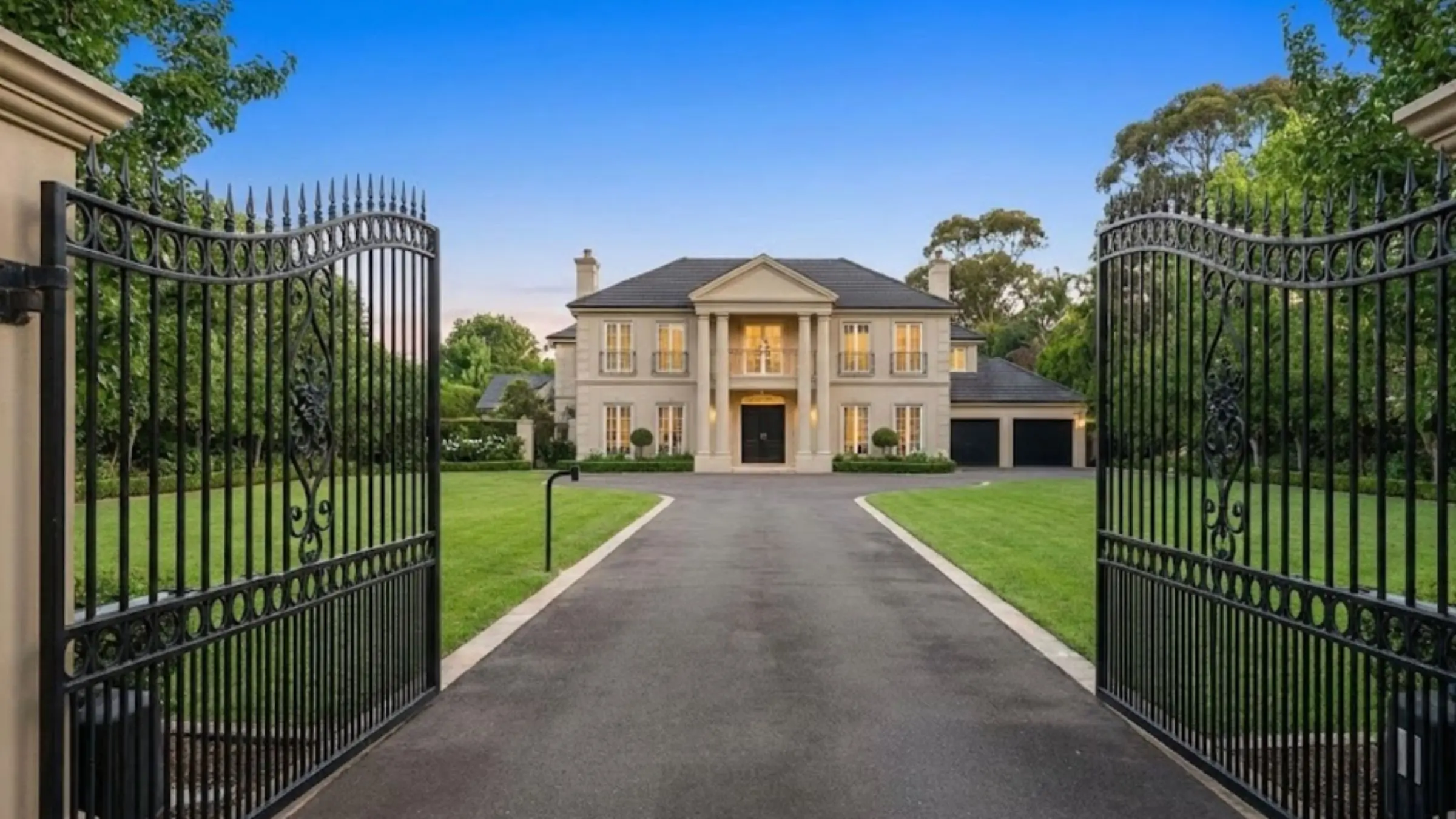 A private, gated entrance with large wrought-iron gates leading up a long driveway to a grand, exclusive estate in Warrawee