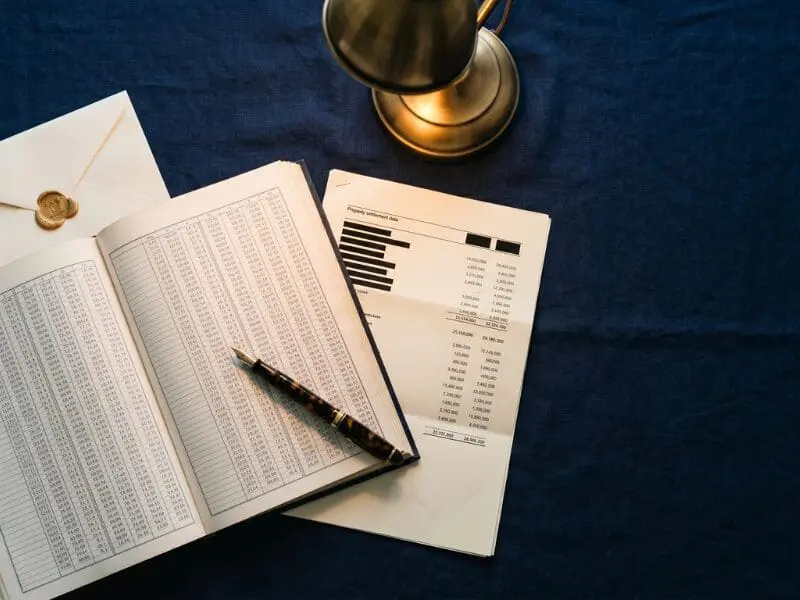 An open ledger of registered property settlement data on a navy linen desk, lit by a brass library lamp — the source dataset behind Sarah Kaye & Co Research