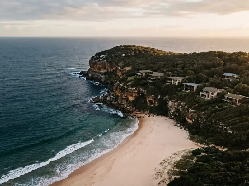 Aerial view of a Northern Beaches headland and coastline at early-morning golden hour — the 57-suburb area covered by Sarah Kaye & Co Research across Sydney's Northern Suburbs