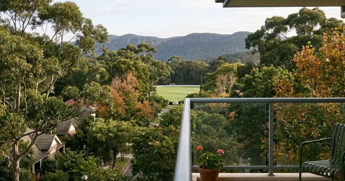 Balcony view from an Upper North Shore apartment looking across mature trees toward a sports oval and the edge of Ku-ring-gai Chase National Park