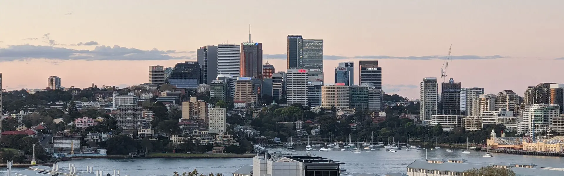 North Sydney office towers and apartment buildings rising above the harbour foreshore and moored boats at dusk