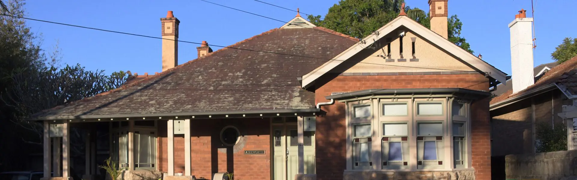 A red-brick Federation cottage with a tiled roof and tall chimneys on a residential street in Willoughby